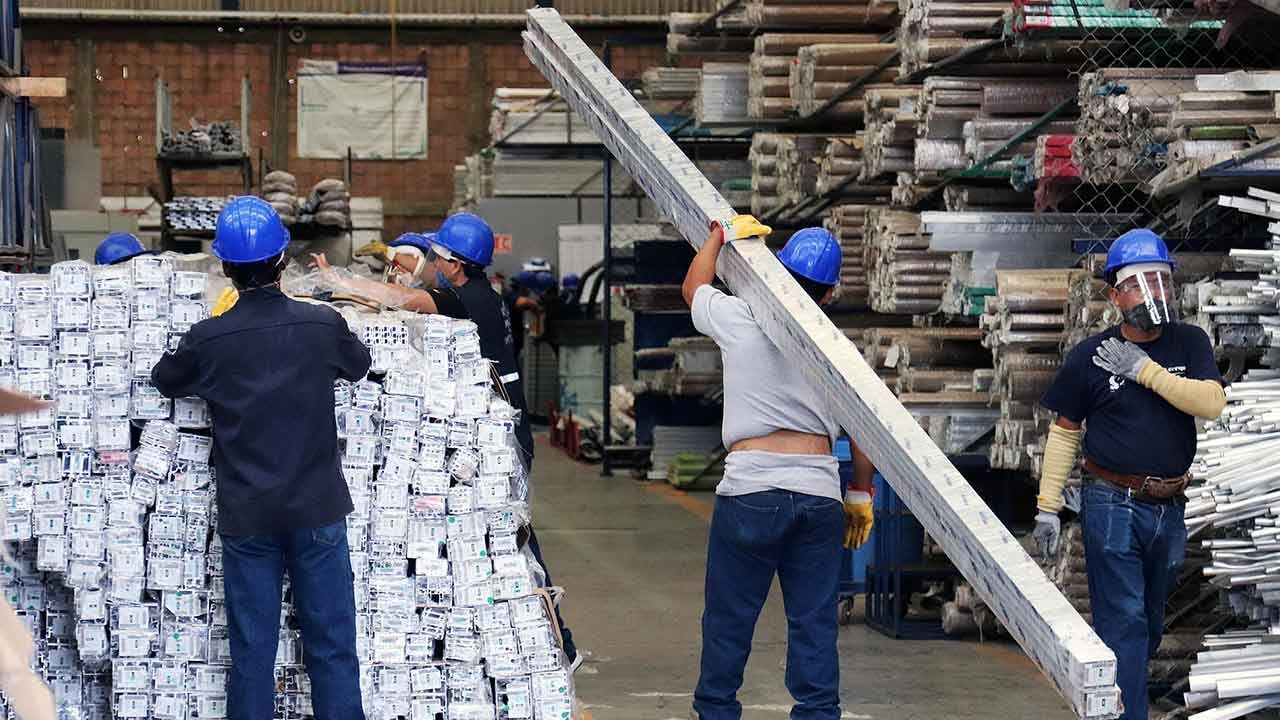 Grupo de trabajadores con cascos azules manejando materiales en un almacén industrial.