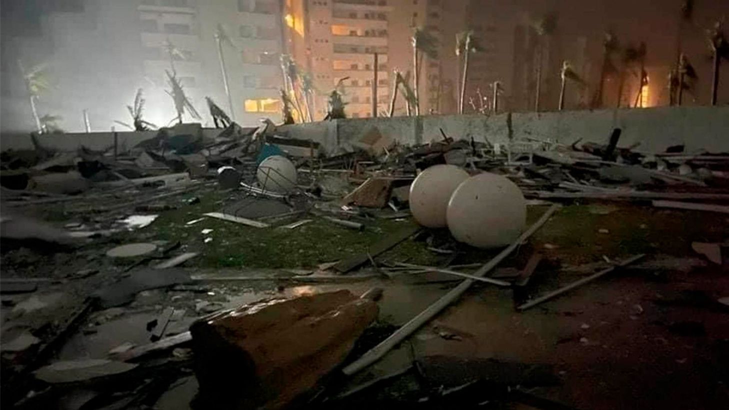 La imagen muestra una escena de destrucción nocturna con escombros y esferas blancas
