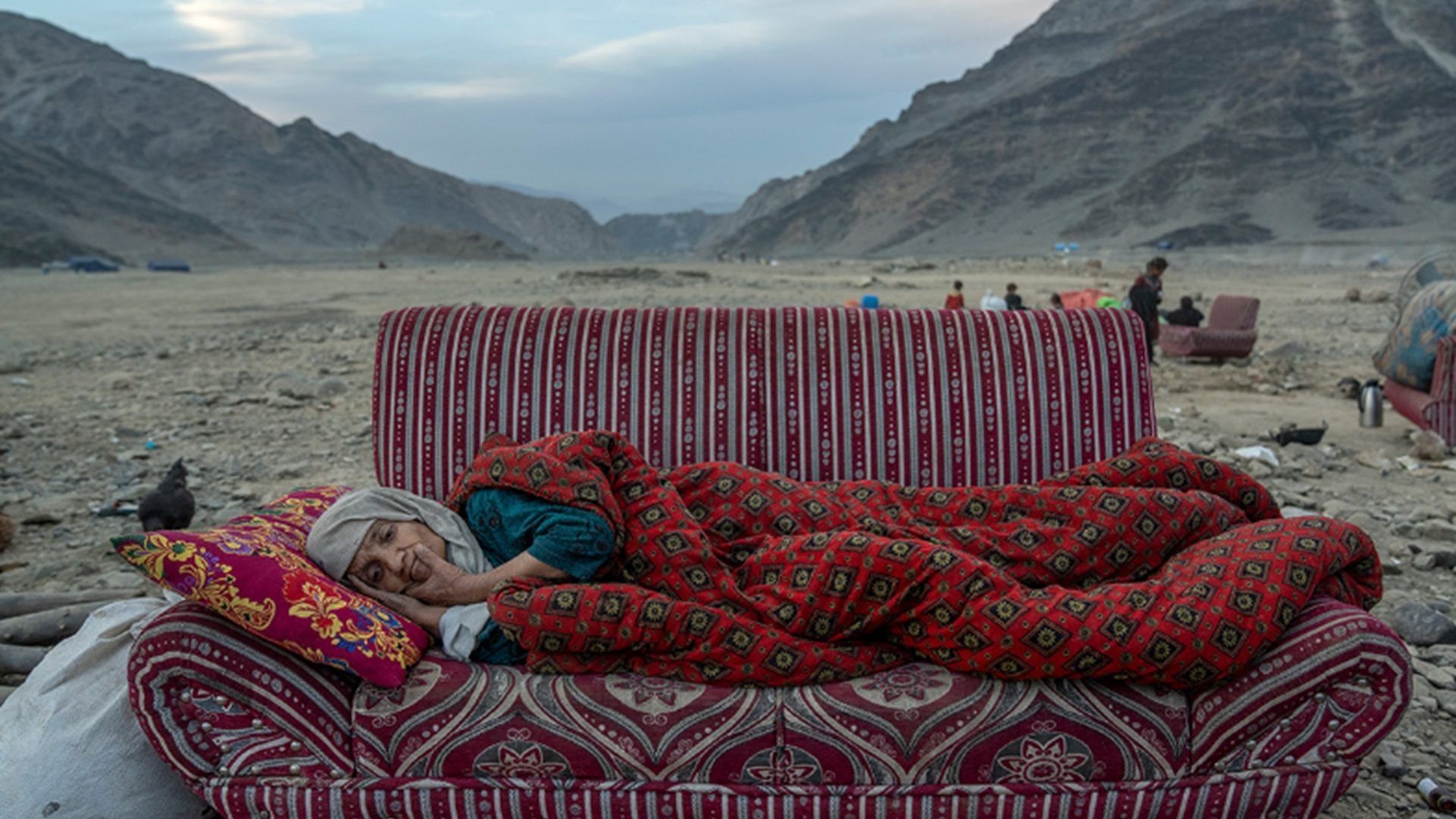 Una mujer afgana descansa en el desierto cerca de un campamento que alberga a personas recientemente deportadas de Pakistán, en Torkham, Afganistán